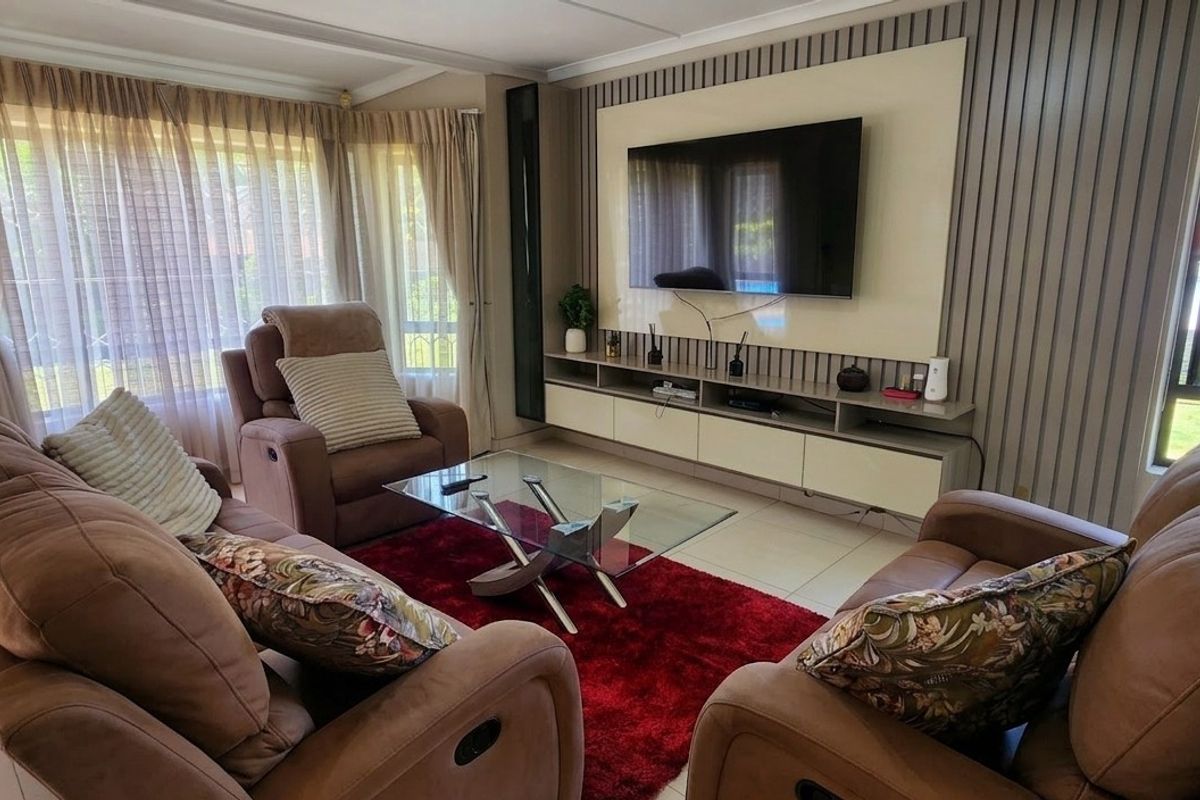 A well-maintained living room featuring a modern built-in media console, decorative slatted wall paneling, and large windows providing ample natural light.