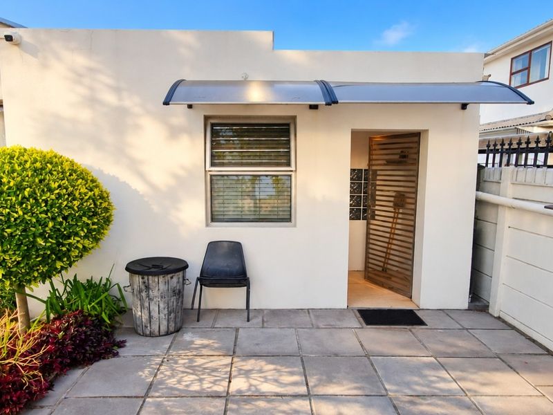 A neat rear exterior view of the cottage featuring a paved patio area, security gate, and protective awning over the entrance.