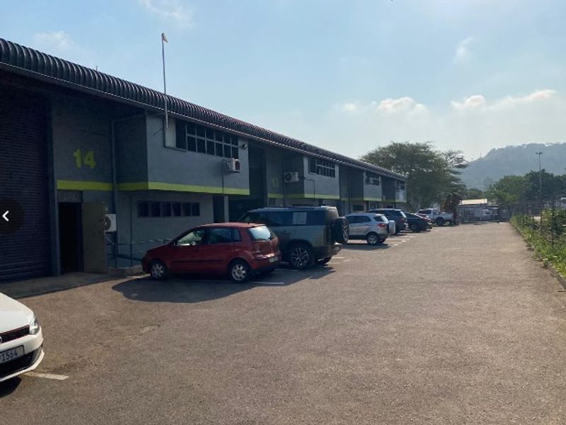 Exterior view of an industrial warehouse complex featuring roller shutter doors, paved parking area, and wall-mounted air conditioning units.