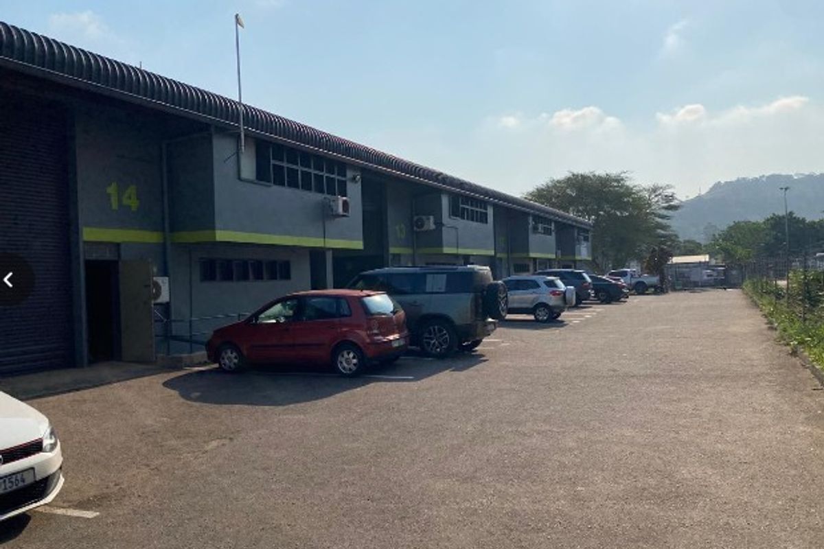 Exterior view of an industrial warehouse complex featuring roller shutter doors, paved parking area, and wall-mounted air conditioning units.