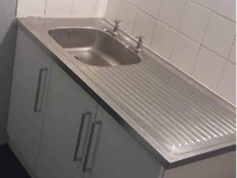 A functional scullery or utility area featuring a stainless steel sink, built-in cabinetry, and a tiled splashback.