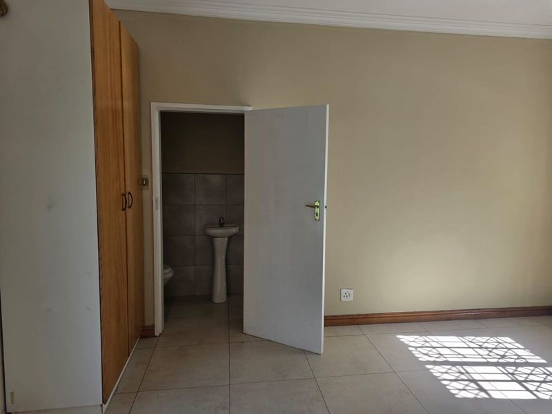 A spacious bedroom featuring tiled flooring, a built-in wardrobe, and an en-suite bathroom with a pedestal basin and toilet.