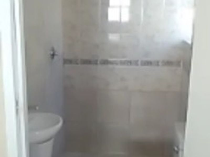 A compact bathroom featuring a pedestal basin, toilet, and a tiled shower area with a curtain rod.