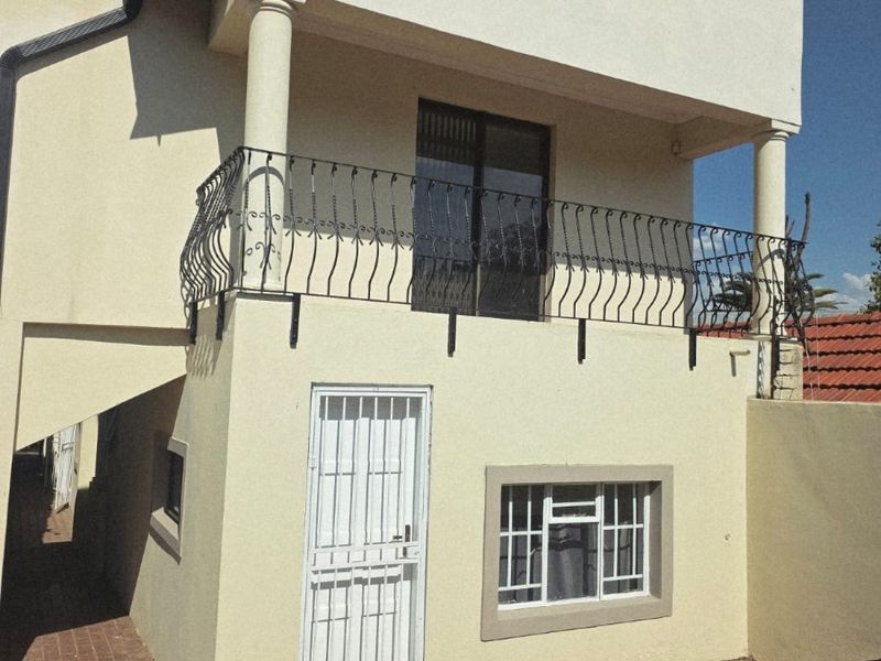 Rear view of the cottage featuring a balcony with wrought iron balustrade, security gates, and paved outdoor area.
