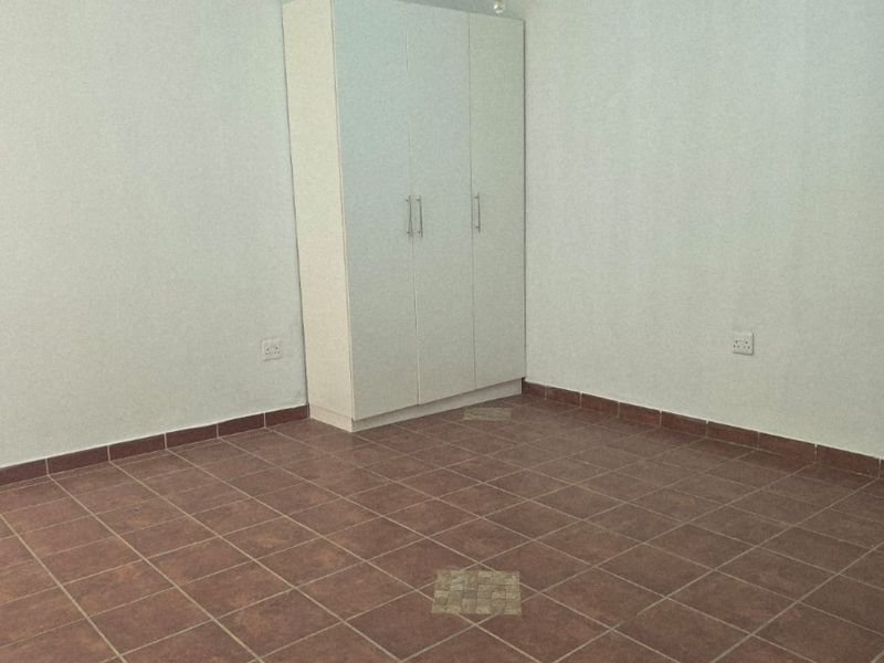 A spacious, empty bedroom featuring tiled flooring, a built-in wardrobe, and a central chandelier fixture.