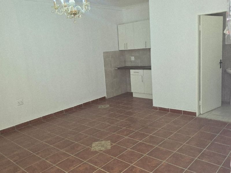 An open-plan living area featuring tiled flooring, a compact kitchen corner with built-in cabinetry, and a decorative chandelier.
