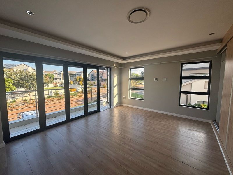 A bright and spacious bedroom featuring modern laminate flooring, built-in cupboards, recessed lighting, and large sliding doors opening to a balcony.