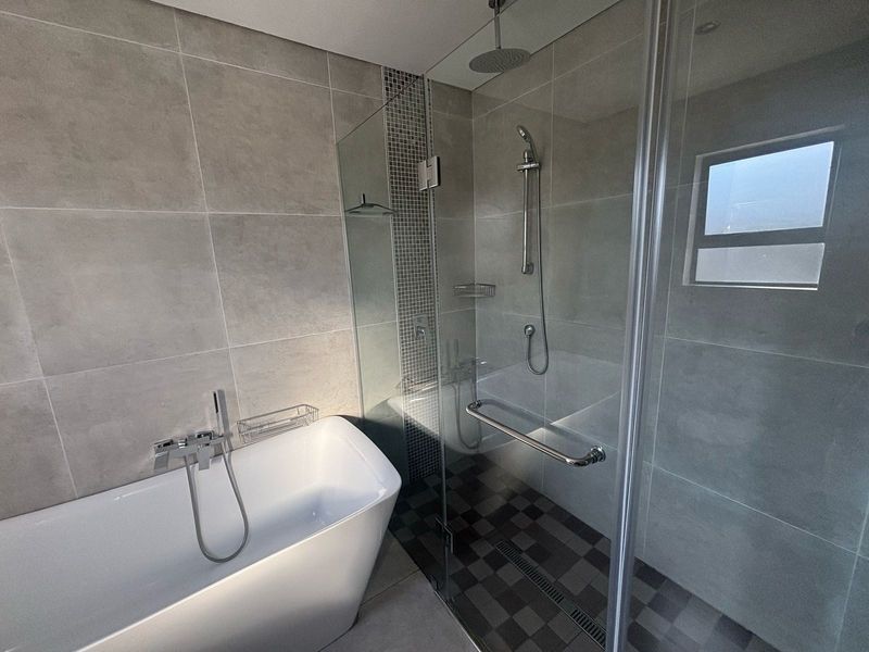 Modern bathroom featuring a sleek freestanding bathtub, a spacious walk-in shower with a rain shower head, and contemporary large-format tiling.