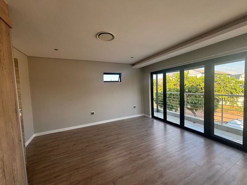 Spacious, modern bedroom featuring laminate flooring, recessed lighting, and large sliding glass doors opening onto a private balcony.