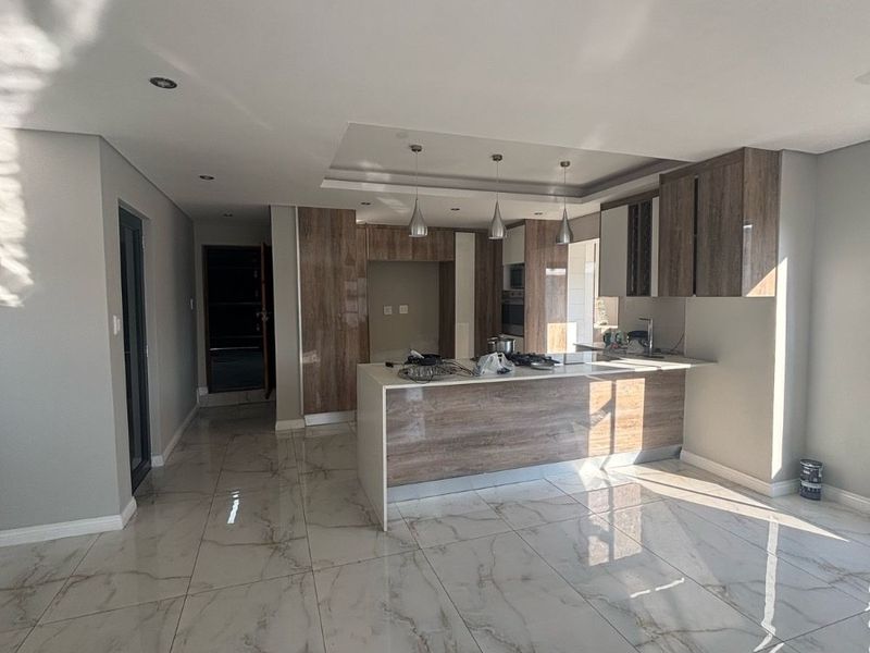 Modern open-plan kitchen featuring sleek wood-finish cabinetry, a central island, and polished marble-look floor tiles with recessed and pendant lighting.