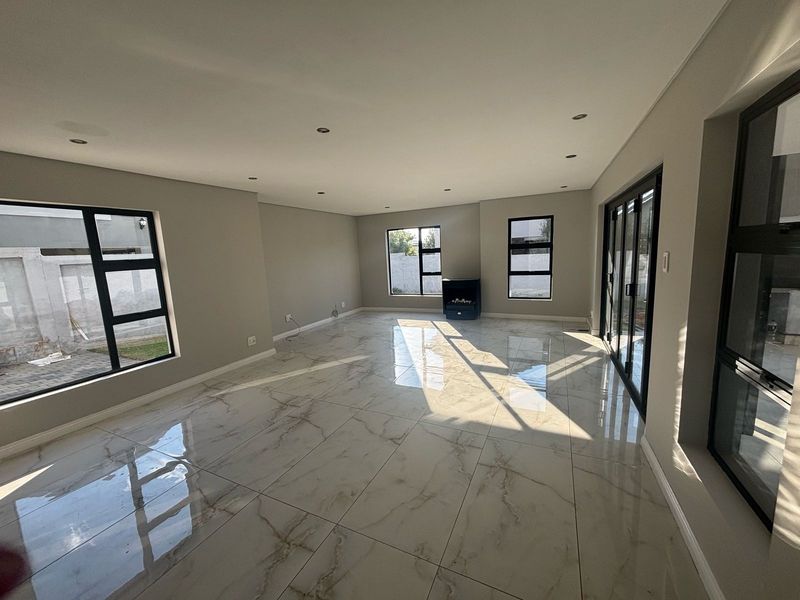 A bright, spacious, and modern living area featuring large porcelain floor tiles, recessed lighting, and expansive aluminium-framed windows and sliding doors.