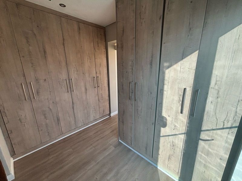 A modern bedroom dressing area featuring extensive built-in wooden cupboards and high-quality laminate flooring with recessed lighting.