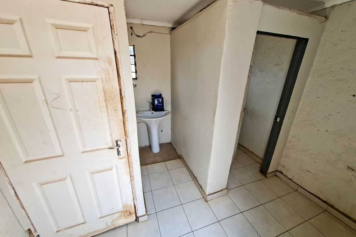 A small, empty bathroom featuring a pedestal basin, tiled flooring, and internal doors, currently requiring cosmetic refurbishment and wall repairs.