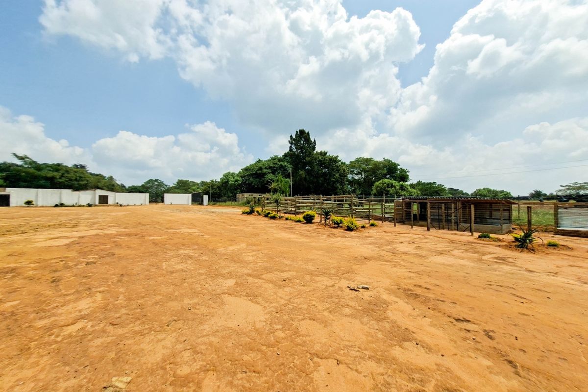 Expansive outdoor area on a small holding featuring fencing, an animal enclosure, and an outbuilding set against a clear sky.