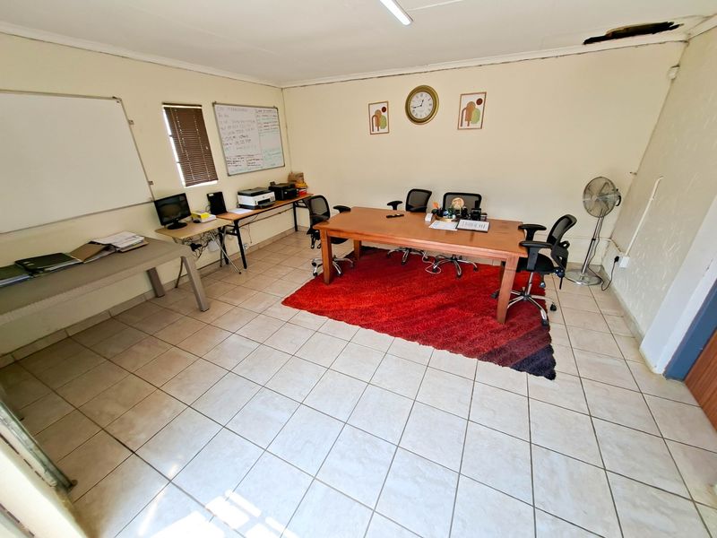 A functional office space featuring tiled flooring and natural light through venetian blinds, currently utilized as a workspace.