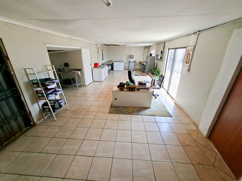 A spacious utility or multi-purpose room featuring tiled flooring, sliding door access, and exposed electrical conduit, suitable for conversion or workshop use.