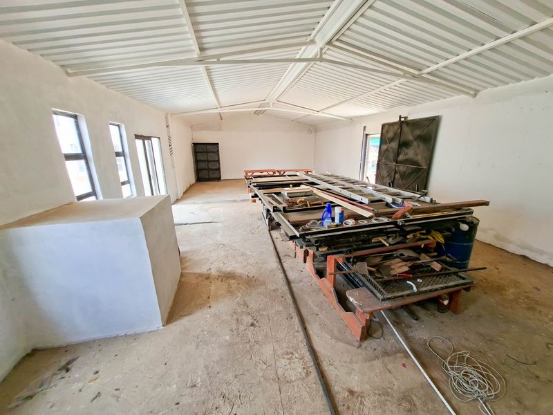A large, open-plan utility or workshop space featuring exposed steel roof trusses, concrete flooring, and large sliding metal doors, suitable for various industrial or storage uses.