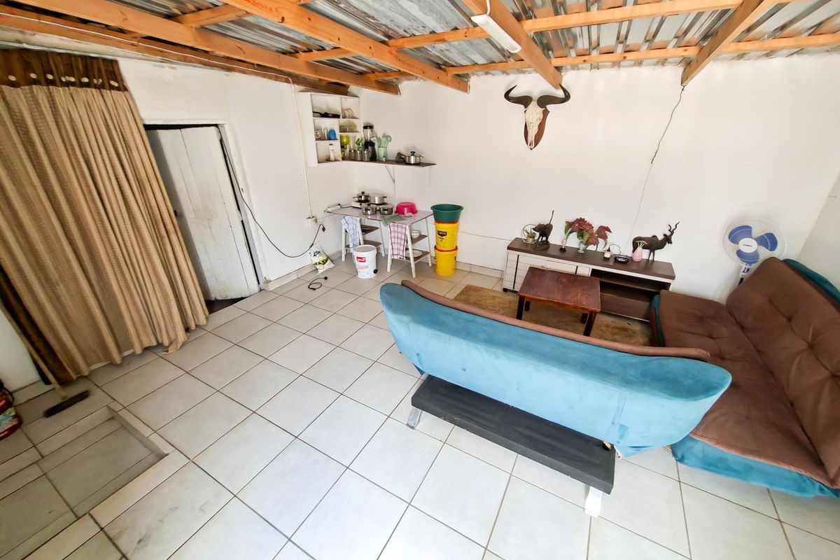 A living area featuring exposed timber roof trusses, corrugated metal ceiling, and ceramic floor tiles, requiring maintenance and cosmetic updates.