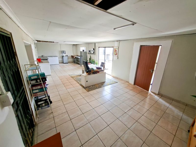 A spacious utility area featuring tiled flooring and a sliding glass door, currently utilized as a workspace with potential for renovation or repurposing.