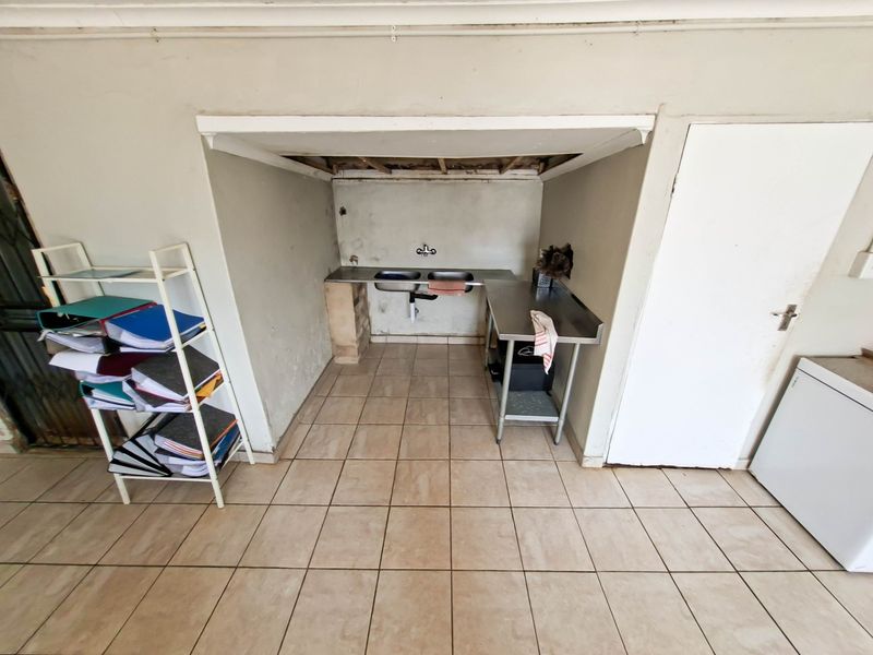 A functional scullery area featuring a double stainless steel sink and tiled flooring, currently requiring ceiling repairs and cosmetic wall maintenance.