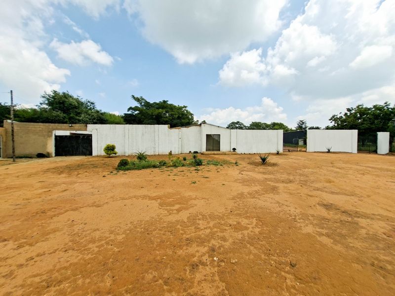 Front view of the property featuring a long perimeter wall, gated entrance, and a large unpaved driveway area.