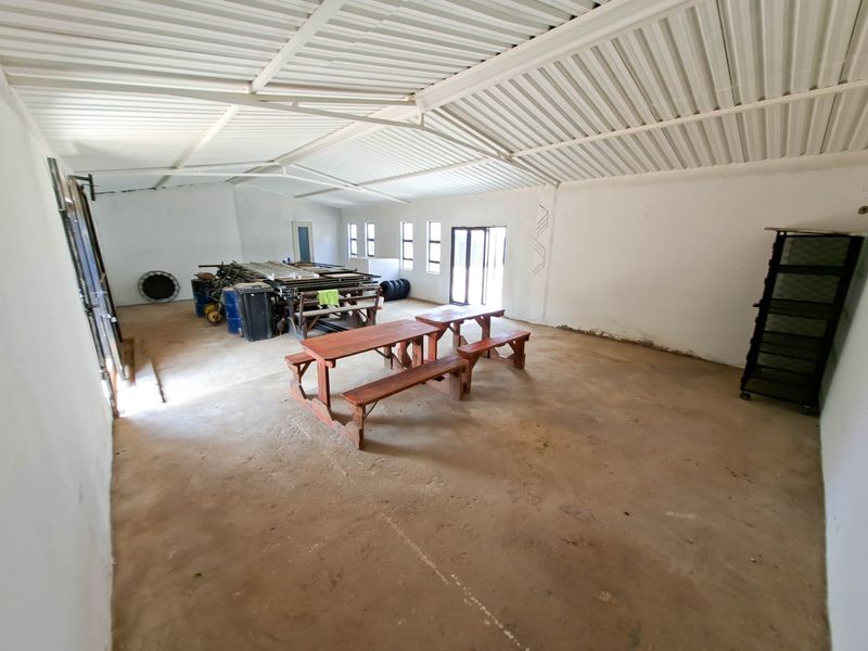 A large, open-plan utility space featuring exposed steel roof trusses, concrete flooring, and ample natural light, suitable for storage or workshop conversion.
