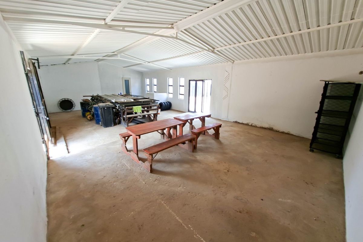 A large, open-plan utility space featuring exposed steel roof trusses, concrete flooring, and ample natural light, suitable for storage or workshop conversion.