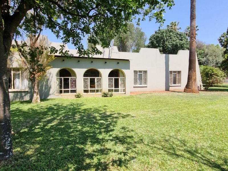 Rear view of the property featuring a well-maintained garden, mature trees, and a building facade with distinctive arched windows and parapet detailing.