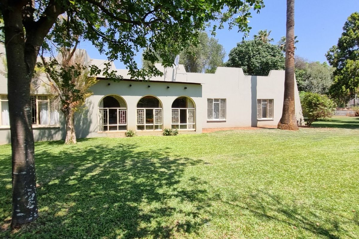 Rear view of the property featuring a well-maintained garden, mature trees, and a building facade with distinctive arched windows and parapet detailing.