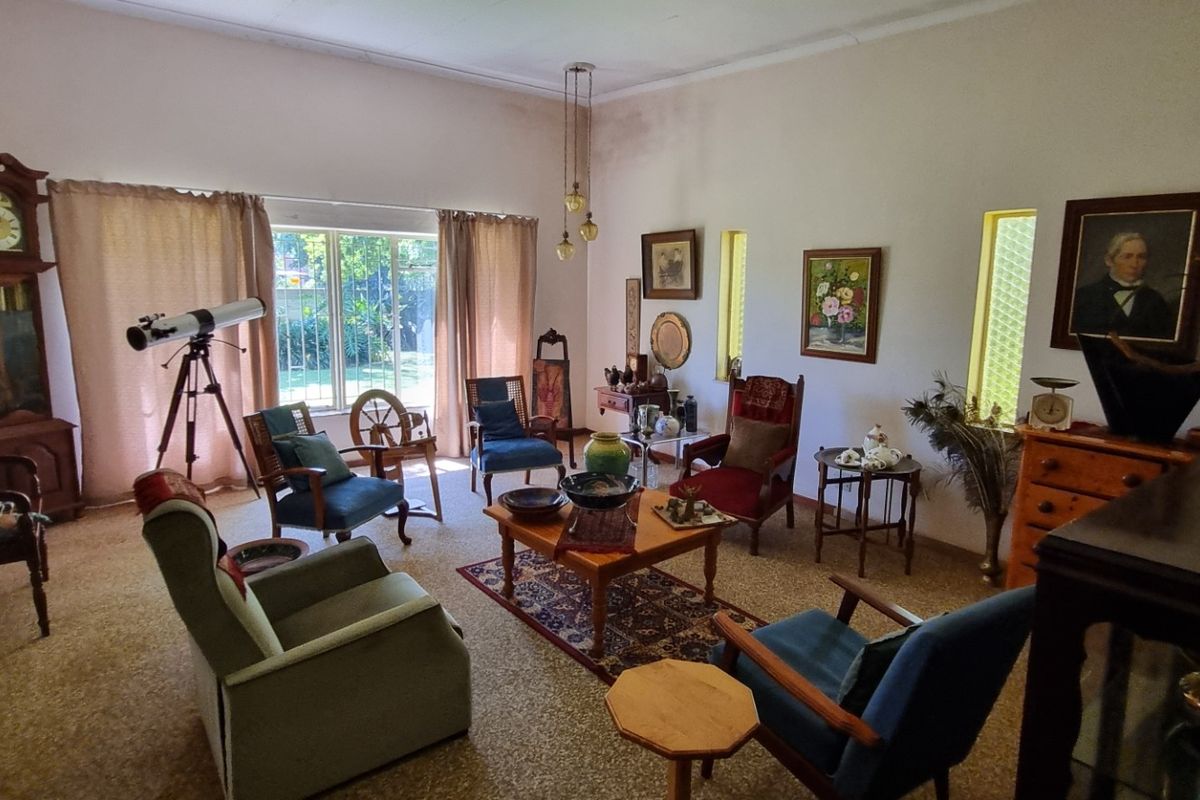 A spacious living room featuring large windows, carpeted flooring, and coved ceilings, currently showing signs of wear and ceiling staining.