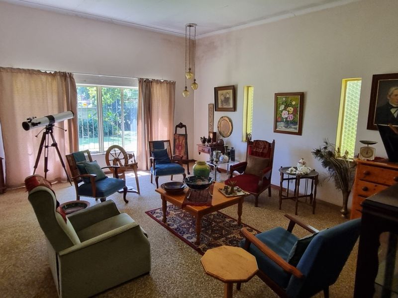 A spacious living room featuring large windows, carpeted flooring, and coved ceilings, currently showing signs of wear and ceiling staining.