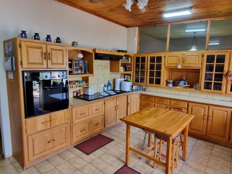 A traditional kitchen featuring extensive wooden cabinetry, built-in oven, extractor fan, and tiled flooring, with a warm wooden ceiling finish.