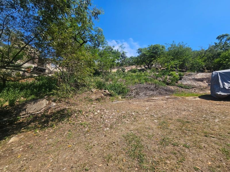 A sloped residential plot featuring natural rock formations and established trees, offering a rugged landscape setting.