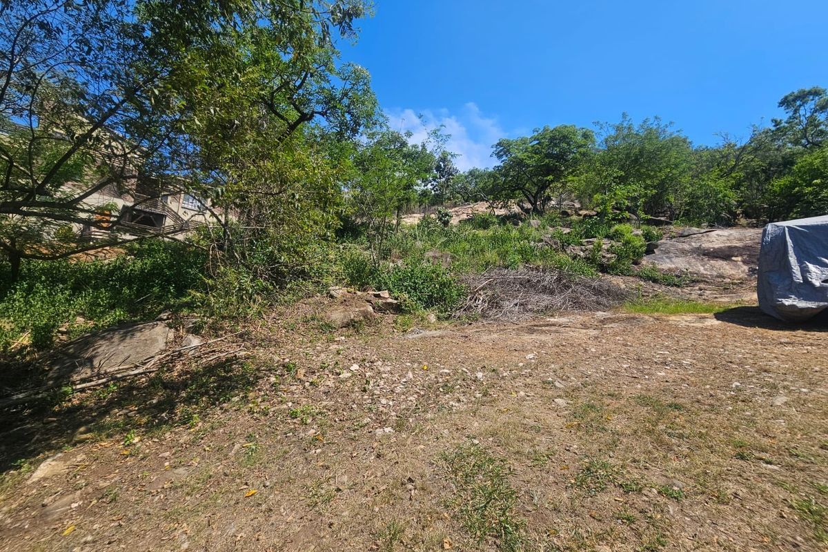 A sloped residential plot featuring natural rock formations and established trees, offering a rugged landscape setting.