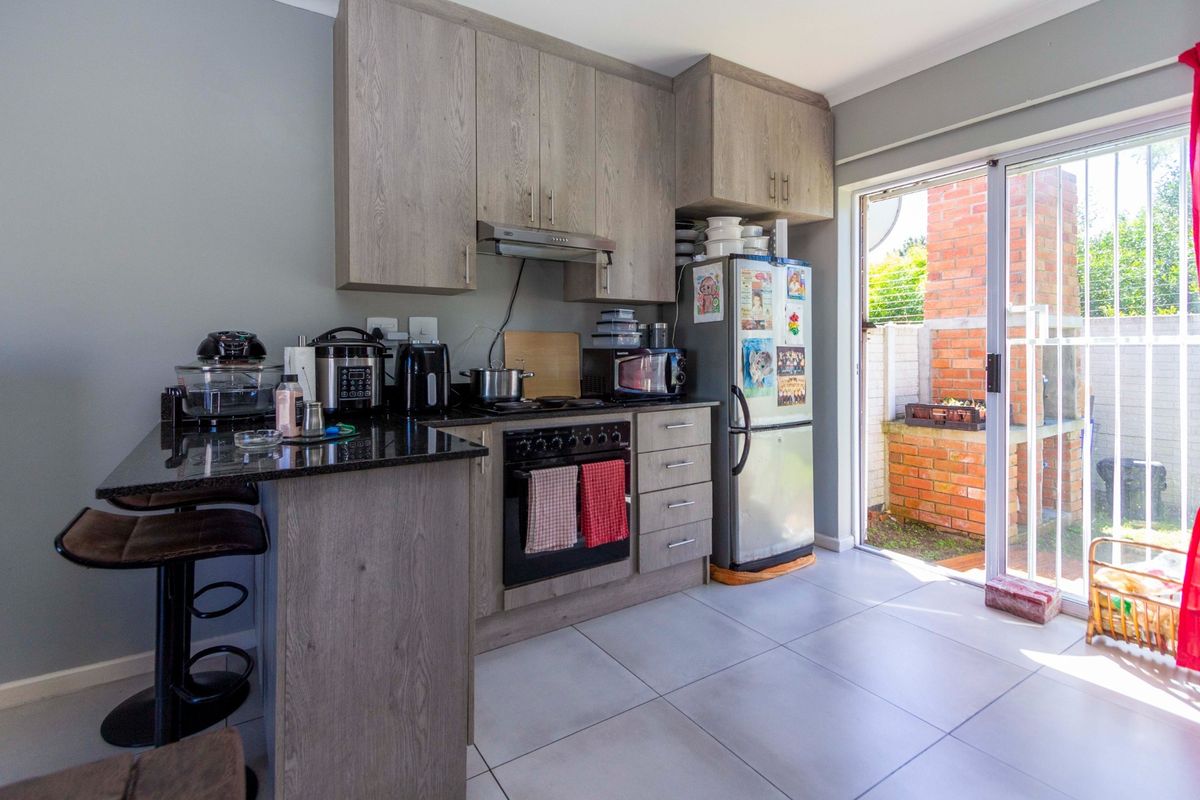 Compact kitchen featuring wood-look cabinetry, granite countertops, built-in oven and hob, and direct access to an outdoor patio area through a sliding glass door.