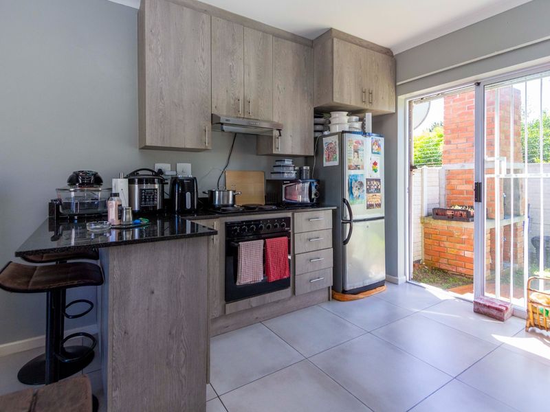Compact kitchen featuring wood-look cabinetry, granite countertops, built-in oven and hob, and direct access to an outdoor patio area through a sliding glass door.
