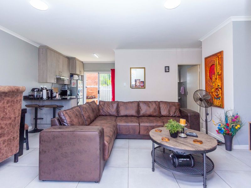 An open-plan living and kitchen area featuring tiled flooring, modern cabinetry, a breakfast bar, and direct access to an outdoor space via sliding doors.