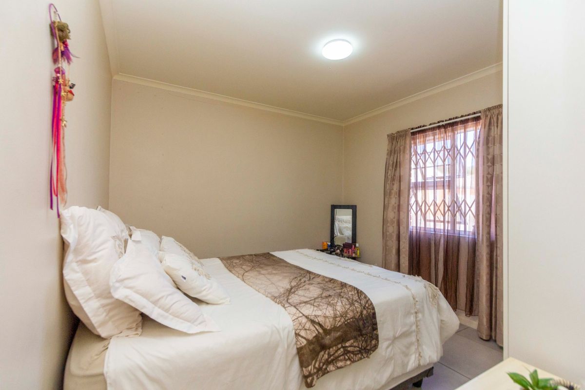 A functional bedroom featuring tiled flooring, a security gate on the window, and a central ceiling light fixture.