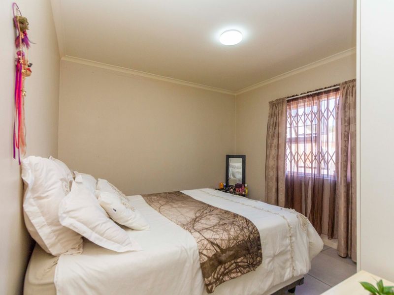 A functional bedroom featuring tiled flooring, a security gate on the window, and a central ceiling light fixture.