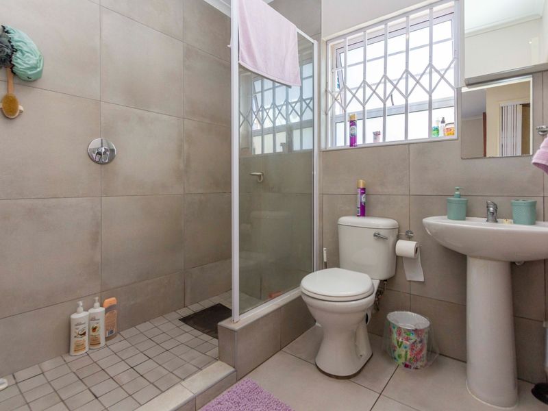 A functional bathroom featuring a walk-in shower with a glass screen, pedestal basin, and toilet, finished with neutral wall and floor tiles.