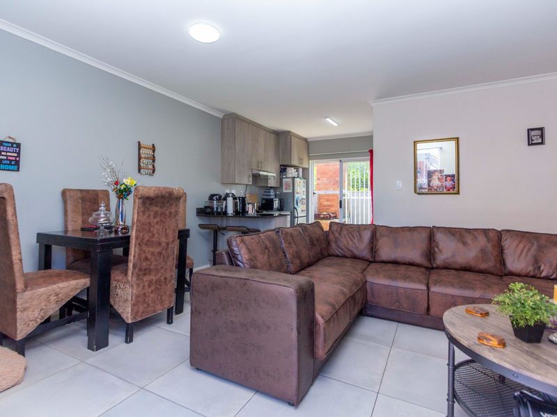 Open-plan living and dining area featuring tiled flooring, recessed lighting, and a compact kitchen with built-in cabinetry and direct access to the rear exterior.
