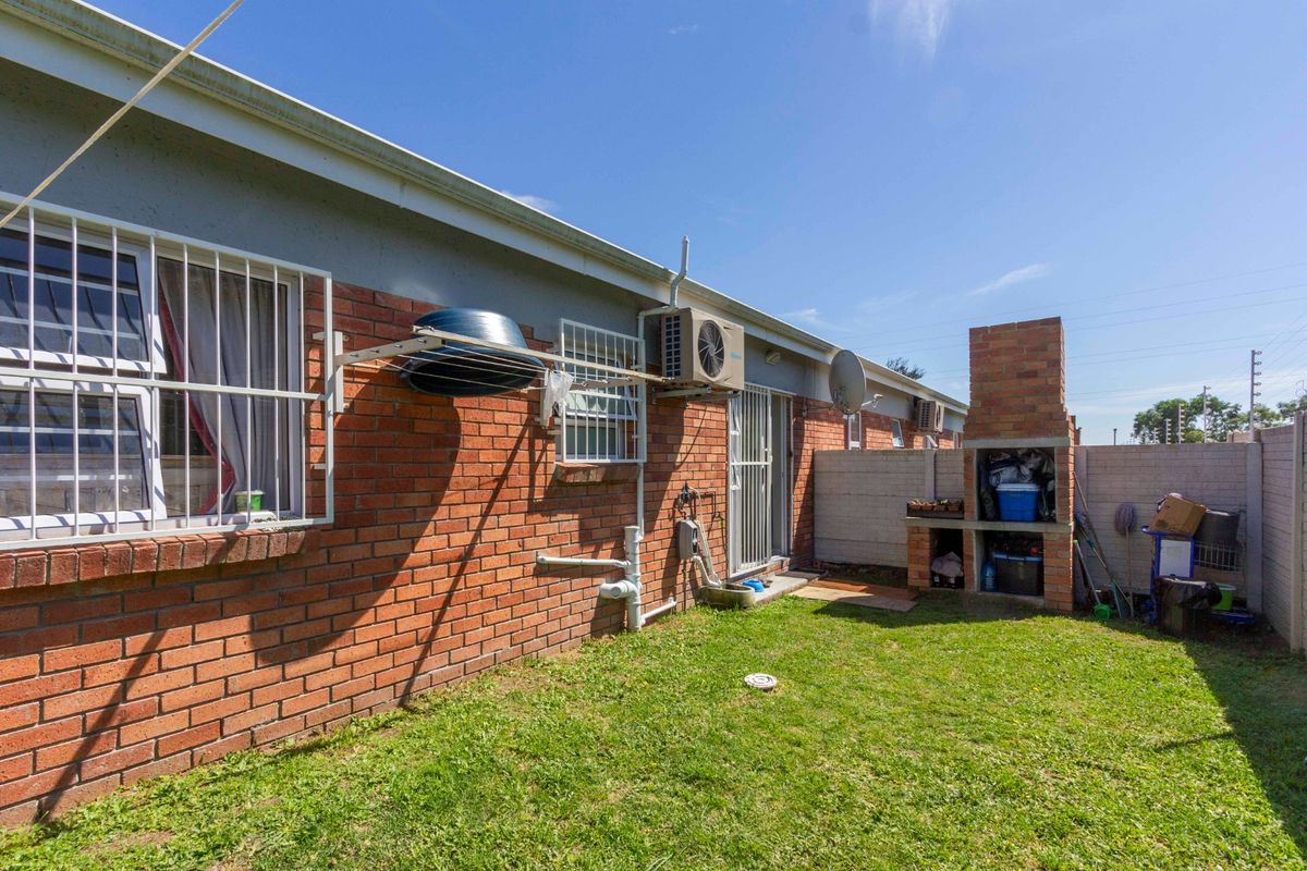 Rear exterior view of the townhouse featuring a small lawn, built-in brick braai, and security-fitted windows.