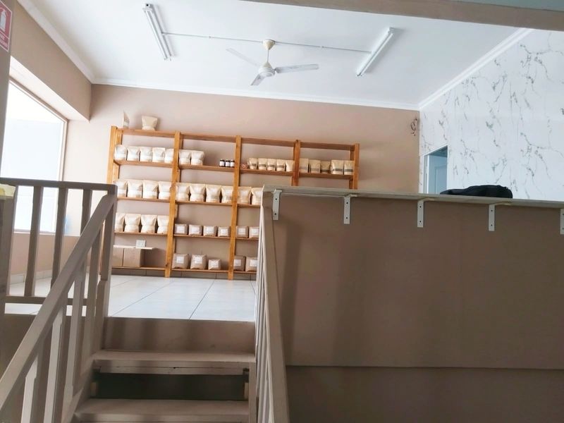 Open plan commercial space featuring a wooden staircase, tiled flooring, ceiling fan, and decorative marble-effect wall paneling.
