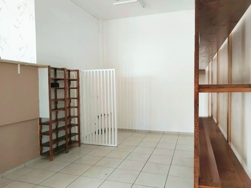 A clean, empty commercial utility space featuring tiled flooring, built-in wooden shelving units, and a decorative slatted room divider.