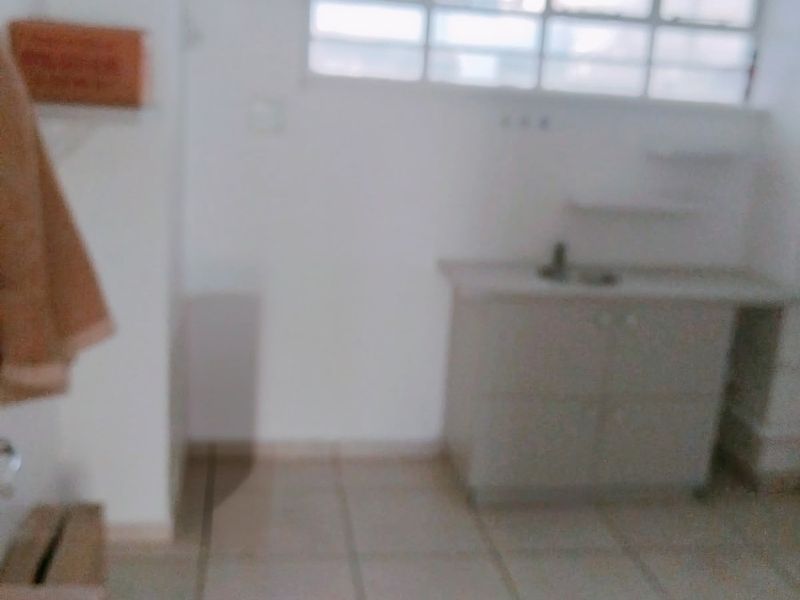 A simple, empty kitchen area featuring tiled flooring, built-in cabinetry with a sink, and a large multi-pane window providing natural light.
