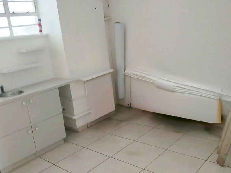 A small, empty kitchen area featuring built-in cabinetry, a sink, and tiled flooring, requiring some maintenance and cosmetic updates.