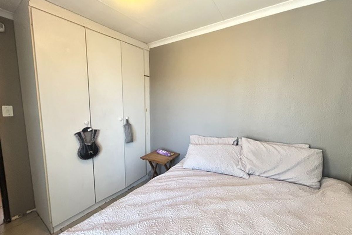 A functional bedroom featuring built-in cupboards, neutral wall finishes, and tiled flooring, offering a practical space for rest.