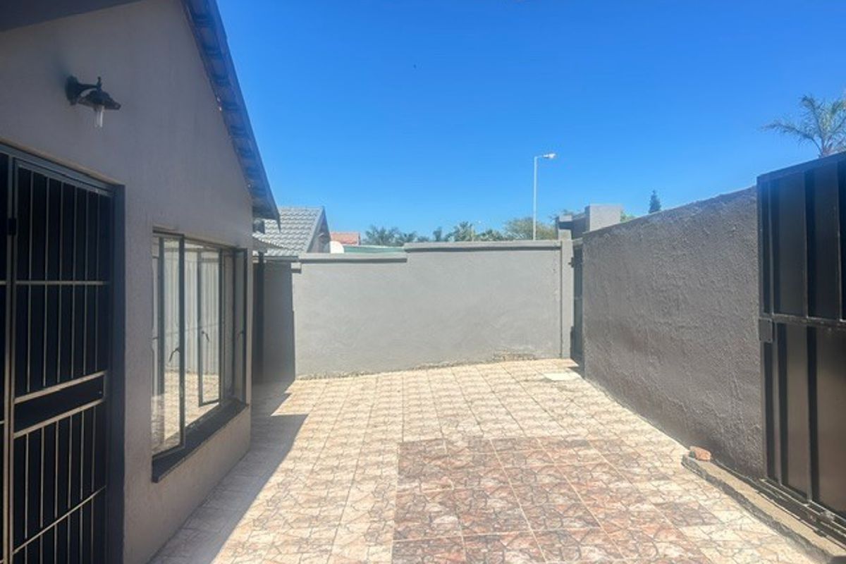 A paved rear courtyard area featuring perimeter walls, security gate access, and exterior lighting, providing a private outdoor space.