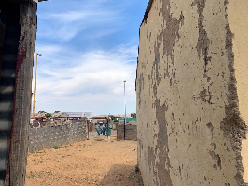 View of the rear yard area showing a boundary wall and significant plaster damage on the exterior building facade.