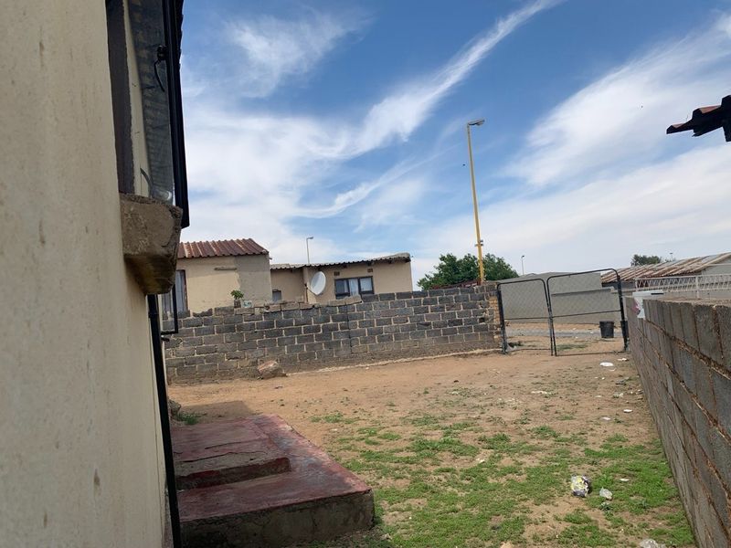 A rear exterior view of the property featuring a concrete block boundary wall, metal gate, and a concrete step leading to the house.